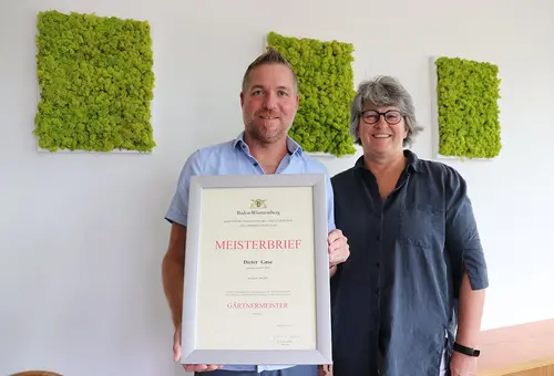 Eine Frau und ein Mann, der seinen Meisterbrief präsentiert.