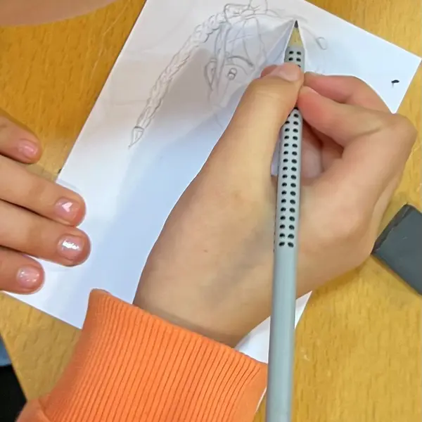 Kinderhand mit Bleistift und dem Entwurf eines Kopfes 