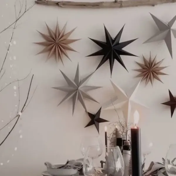 Papiersterne in verschiedenen Farben und Größen hängen an Fäden von einem Zweig herab