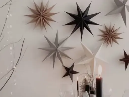 Papiersterne in verschiedenen Farben und Größen hängen an Fäden von einem Zweig herab