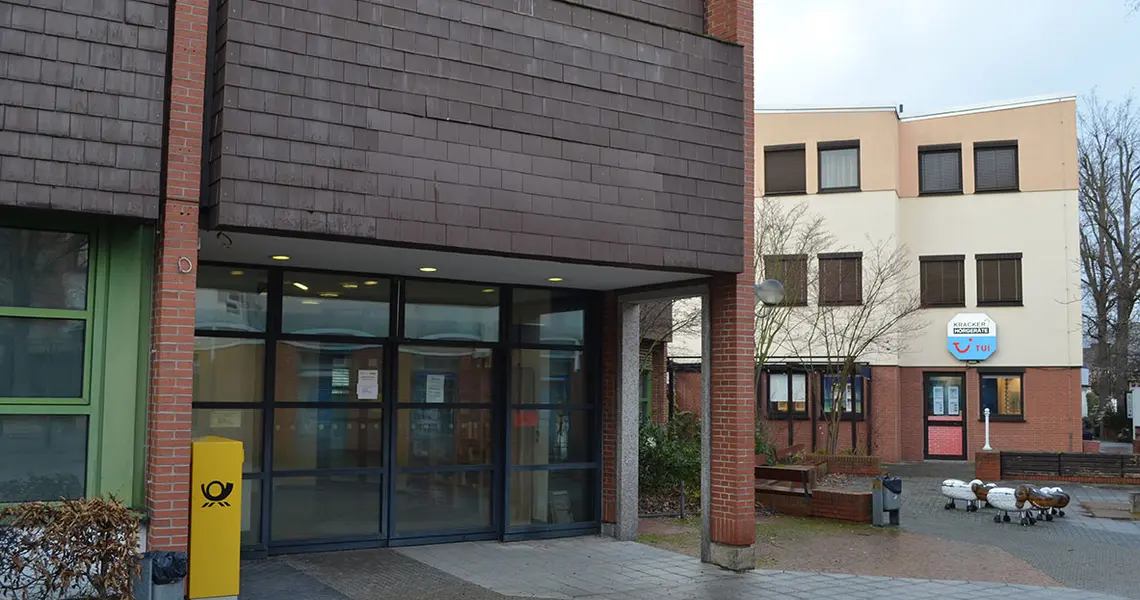 Außenansicht des Eingangsbereiches des alten Postgebäudes am Rathaus mit Sitzbänken und Kleinkinderspielgeräten im Hintergrund