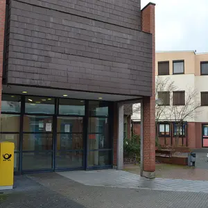 Außenansicht des Eingangsbereiches des alten Postgebäudes am Rathaus mit Sitzbänken und Kleinkinderspielgeräten im Hintergrund