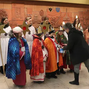11 Sternsinger in Gewändern erhalten von der Bürgermeisterin eine Spende überreicht.