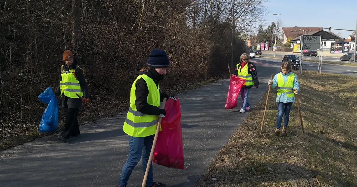 Mehrere Menschen sammeln am Rande eines Radweges Abfälle aus der Natur.
