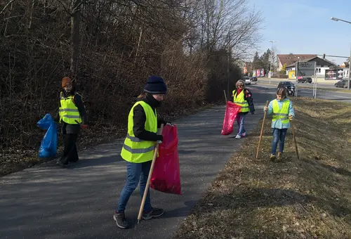 Mehrere Menschen sammeln am Rande eines Radweges Abfälle aus der Natur.