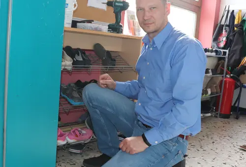 Christoph Degen kniet vor einer Wand, um einen Feuerlöscher anzubringen.