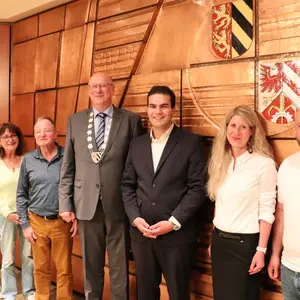 Zwei Frauen und fünf Männer vor der mit Kupfer beschlagenen Wand des Sitzungssaals