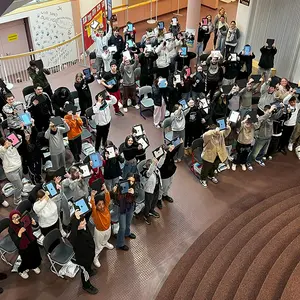 Blick von oben in die Aula, in der viele Schüler ihr Tablet nach oben recken.