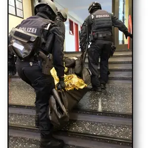 Drei Polizeipersonen in Kampfmontur mit Helm tragen eine Person mit Hilfe einer Rettungsdecke eine Treppe hinauf.