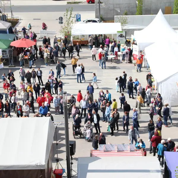 Menschen vor einer Bühne von oben. Rechts im Bild ist das Dach eines Zelts zu sehen.