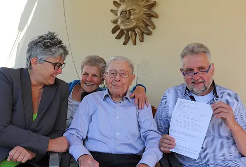 Zwei Männer und zwei FRauen sitzen auf einem Balkon und schauen in die Kamera.