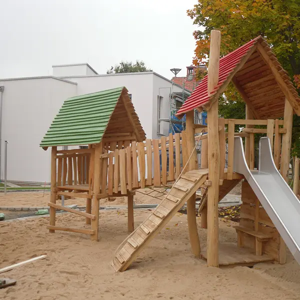 Zwei Klettertürme aus Holz mit einer verbindenden Hängebrücke und einer Rutsche aus Metall