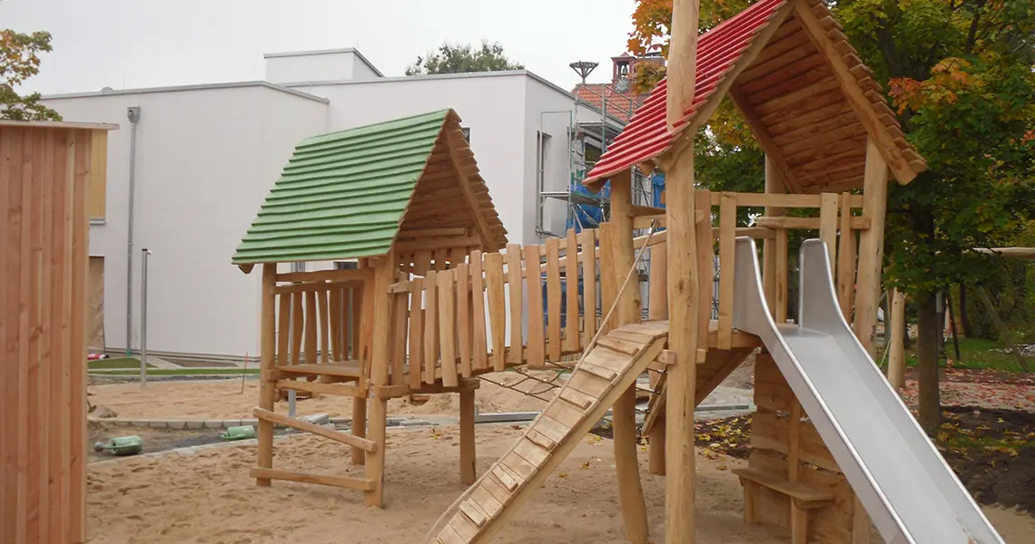 Zwei Klettertürme aus Holz mit einer verbindenden Hängebrücke und einer Rutsche aus Metall