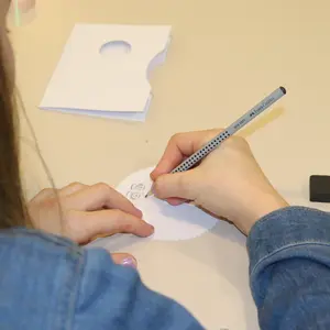 Einem Mädchen beim Zeichnen von hinten über die Schulter fotografiert. Man sieht eine Hand, die einen Bleistift hält. 