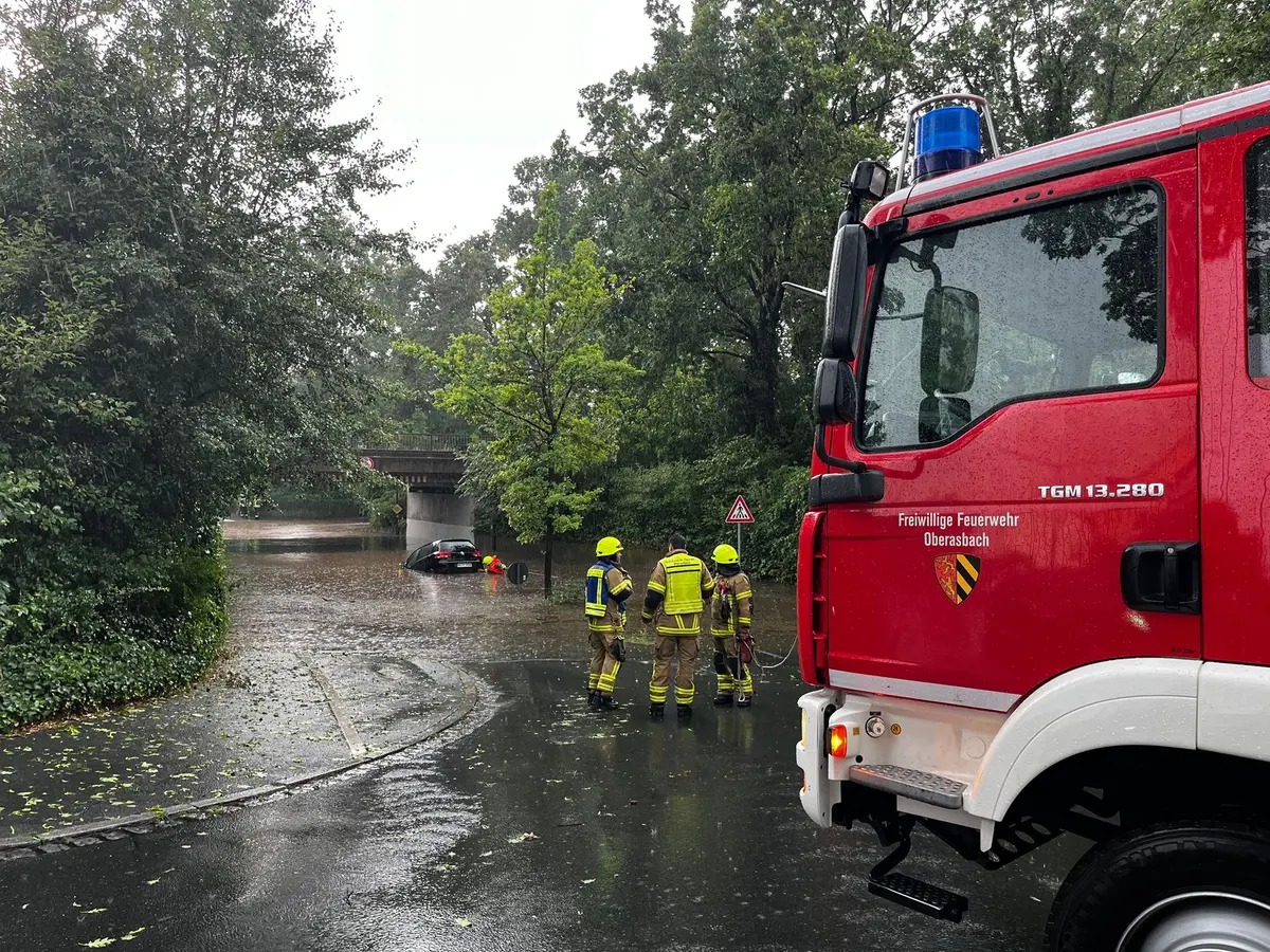 Brücke mit überschwemmter Unterführung. Darin ein Fahrzeug und im Vordergrund das Feuerwehrfahrzeug.