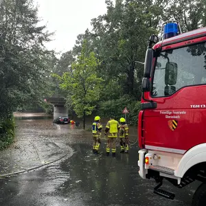 Brücke mit überschwemmter Unterführung. Darin ein Fahrzeug und im Vordergrund das Feuerwehrfahrzeug.