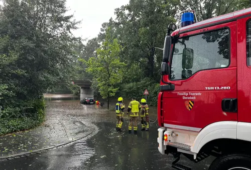 Brücke mit überschwemmter Unterführung. Darin ein Fahrzeug und im Vordergrund das Feuerwehrfahrzeug.