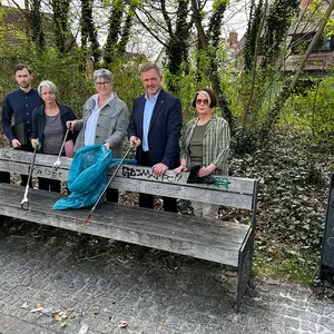 Drei Frauen und zwei Männer stehen hinter einer Parkbank und zeigen ihre Müllbeutel und halten Abfallgreifer hoch.