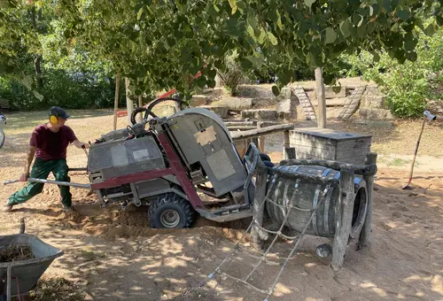 Arbeiter mit Gehörschutz bewegt eine große und schwere Maschine für die Sandreinigung über einen Spielplatz