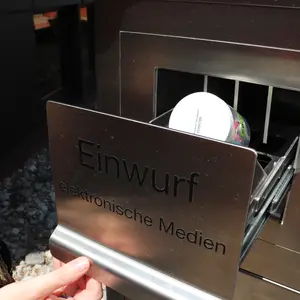 Eine Hand hält die Schublade "Einwurf elektronische Medien" geöffnet. Darin liegt eine durchsichtige Dose mit einem Tonie. 