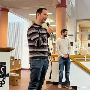 Ein Mann mit Mikrofon und ein weiterer im Hintergrund