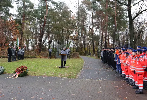 Birgit Huber hält eine Rede auf dem Friedhof. Links und rechts Abordnungen, im Vordergrund ein Kranz.