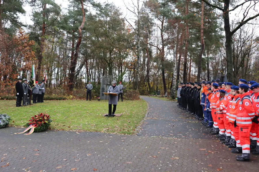 Birgit Huber hält eine Rede auf dem Friedhof. Links und rechts Abordnungen, im Vordergrund ein Kranz.