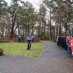 Birgit Huber hält eine Rede auf dem Friedhof. Links und rechts Abordnungen, im Vordergrund ein Kranz.