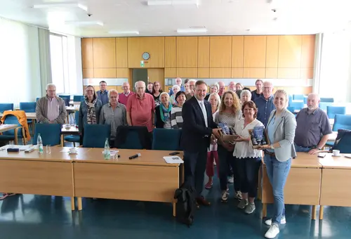 Eine Gruppe von alten Menschen. Es werden zwei Geschenkkörbe überreicht. 