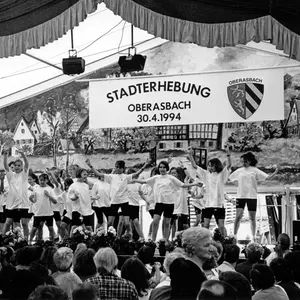 Schwarzweiß-Foto eines Blicks in ein Bierzelt. An der Rückwand hängt eine Tafel mit der Inschrift Stadterhebung Oberasbach 30.4.1994. Daneben das Obearsbacher Wappen.