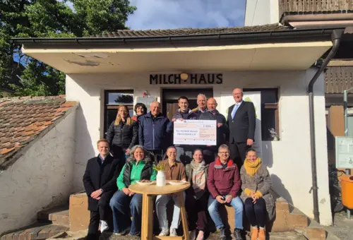 Eine Gruppe von Leuten mit einem PR-Scheck vor einem weißen Häuschen