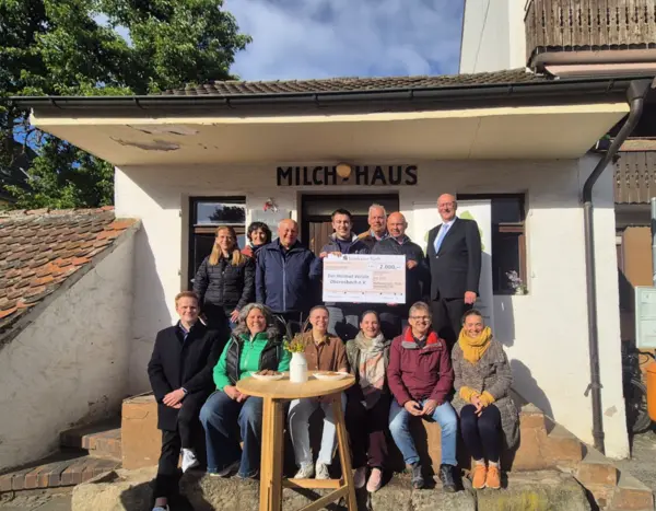 Eine Gruppe von Leuten mit einem PR-Scheck  vor einem weißen Häuschen