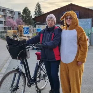 ältere Frau mit Fahrrad, neben ihr eine Frau im Plüschhasenkostüm