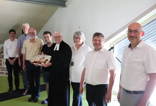Sieben Männer und eine Frau lächeln in die Kamera, wober der Pfarrer im Talar in der MItte einen gebackenen Schlüssel hält.