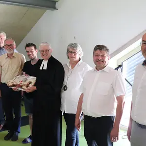 Sieben Männer und eine Frau lächeln in die Kamera, wober der Pfarrer im Talar in der MItte einen gebackenen Schlüssel hält.