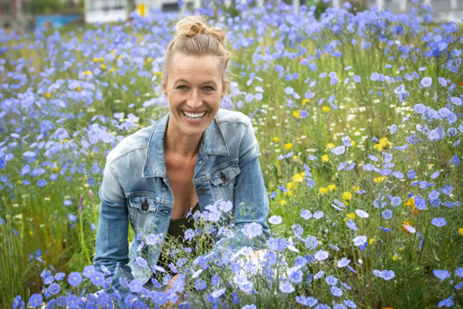 Autorin Nadine Schubert in einer Blumenwiese mit blauen Blumen. Sie trägt eine Jeansjacke und einen hohen Dutt. 