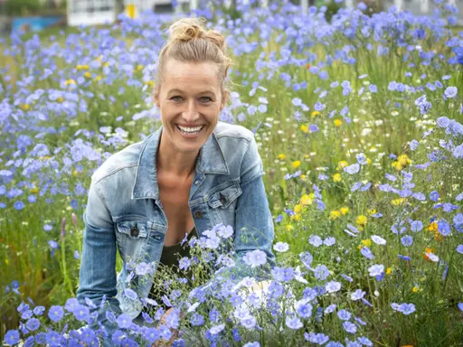 Autorin Nadine Schubert in einer Blumenwiese mit blauen Blumen. Sie trägt eine Jeansjacke und einen hohen Dutt. 