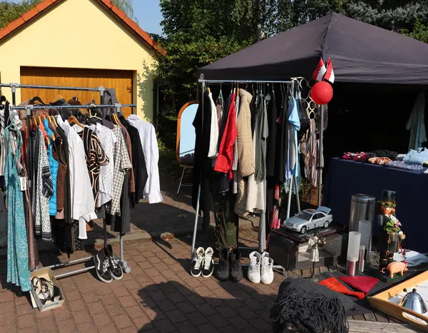 Kleiderstangen mit Second-Hand-Kleidung vor Garage 