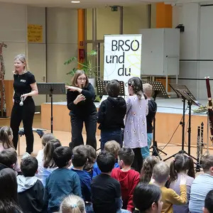 Drei Kinder werden vorne angeleitet auf Wasserflaschen zu spielen. Im Hintergrund die anderen Musiker, im Vordergrund das Pubklikum.