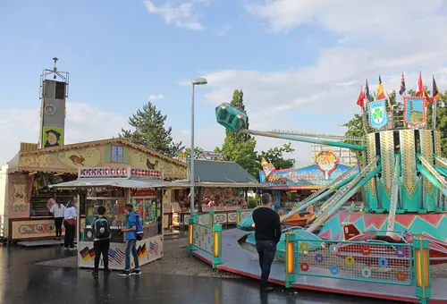 Fahrgeschäfte und BUden im Vordergrung, dahinter der Kirchturm von St. Markus.
