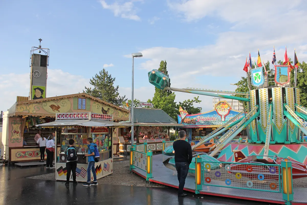 Fahrgeschäfte und BUden im Vordergrung, dahinter der Kirchturm von St. Markus.