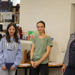 Ein Mädchen bei der Preisübergabe. Im Hintergrund drei Frauen vom Büchereiteam.
