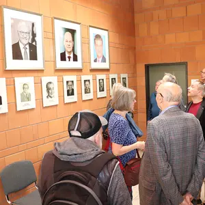 Ein Gruppe Menschen steht vor der Wand mit Porträts.