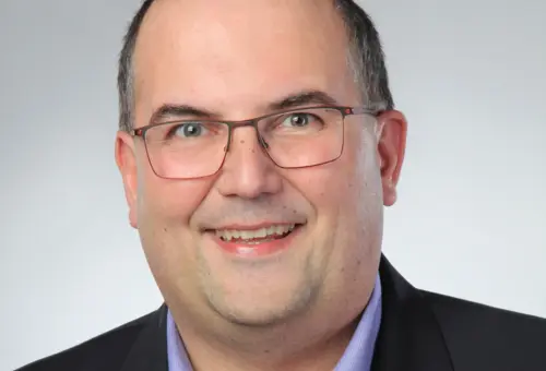 Junger Mann mit Brille, blauem Hemd und schwarzer Anzugjacke