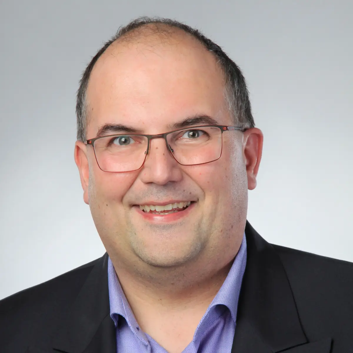 Junger Mann mit Brille, blauem Hemd und schwarzer Anzugjacke