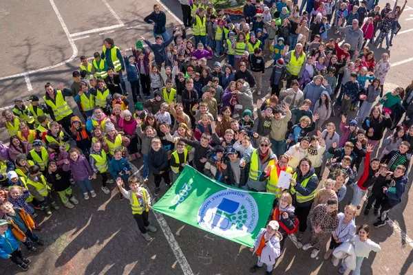 Eine große Menge an Grundschülern mit Eltern und Lehrern, viele in gelben Warnwesten, die eine ausgerollte Fahne halten