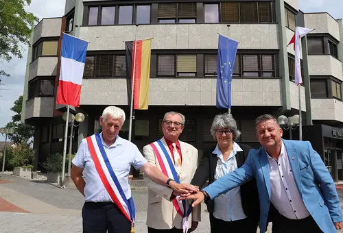Drei Männer und eine Frau stehen vor dem Rathaus und haben ihre Hände wie zum Schwur vor sich zusammengelegt. Im Hintergrund das Rathaus ist mit Flaggen von FRankreich, Deutschland, Europa und Polen geschmückt.aben 