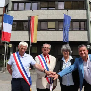 Drei Männer und eine Frau stehen vor dem Rathaus und haben ihre Hände wie zum Schwur vor sich zusammengelegt. Im Hintergrund das Rathaus ist mit Flaggen von FRankreich, Deutschland, Europa und Polen geschmückt.aben 