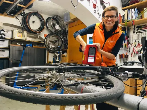 Eine Frau in einer Werkstatt codiert ein Fahrrad mit einem Codiergerät. Das Foto ist über das Vorderrad hinweg aufgenommen 