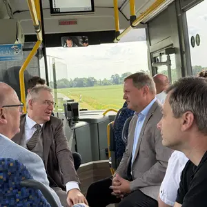 Blick auf das Innere eines Linienbusses: von hinten auf die vorderen Sitzreihen und durch die Windschutzscheibe. Vier Männer sitzen sich gegenüber und unterhalten sich.